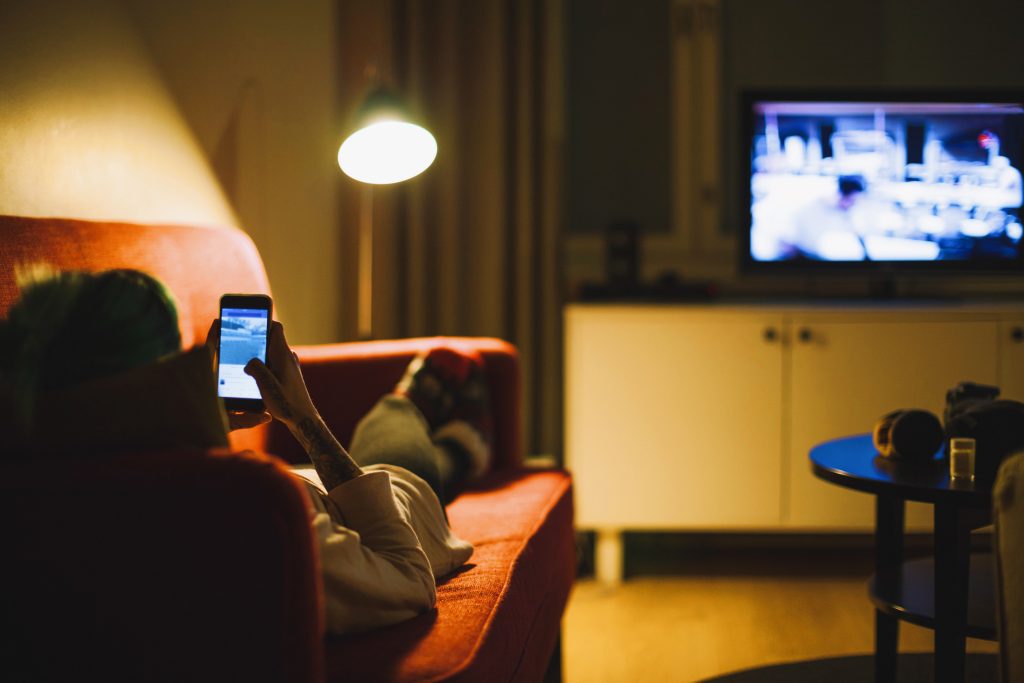 Young woman relaxing with a smartphone while watching television. (Getty Images)