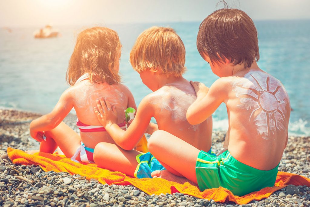 Three kids applying sunscreen to each other on the beach