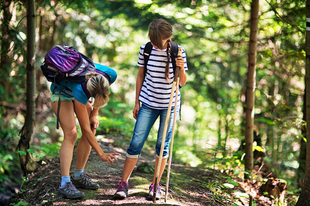 Mother spraying insect repellent on daughter in woods