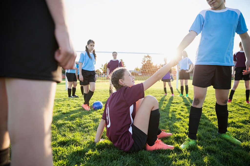 Teen girl helping opponent up on the soccer field