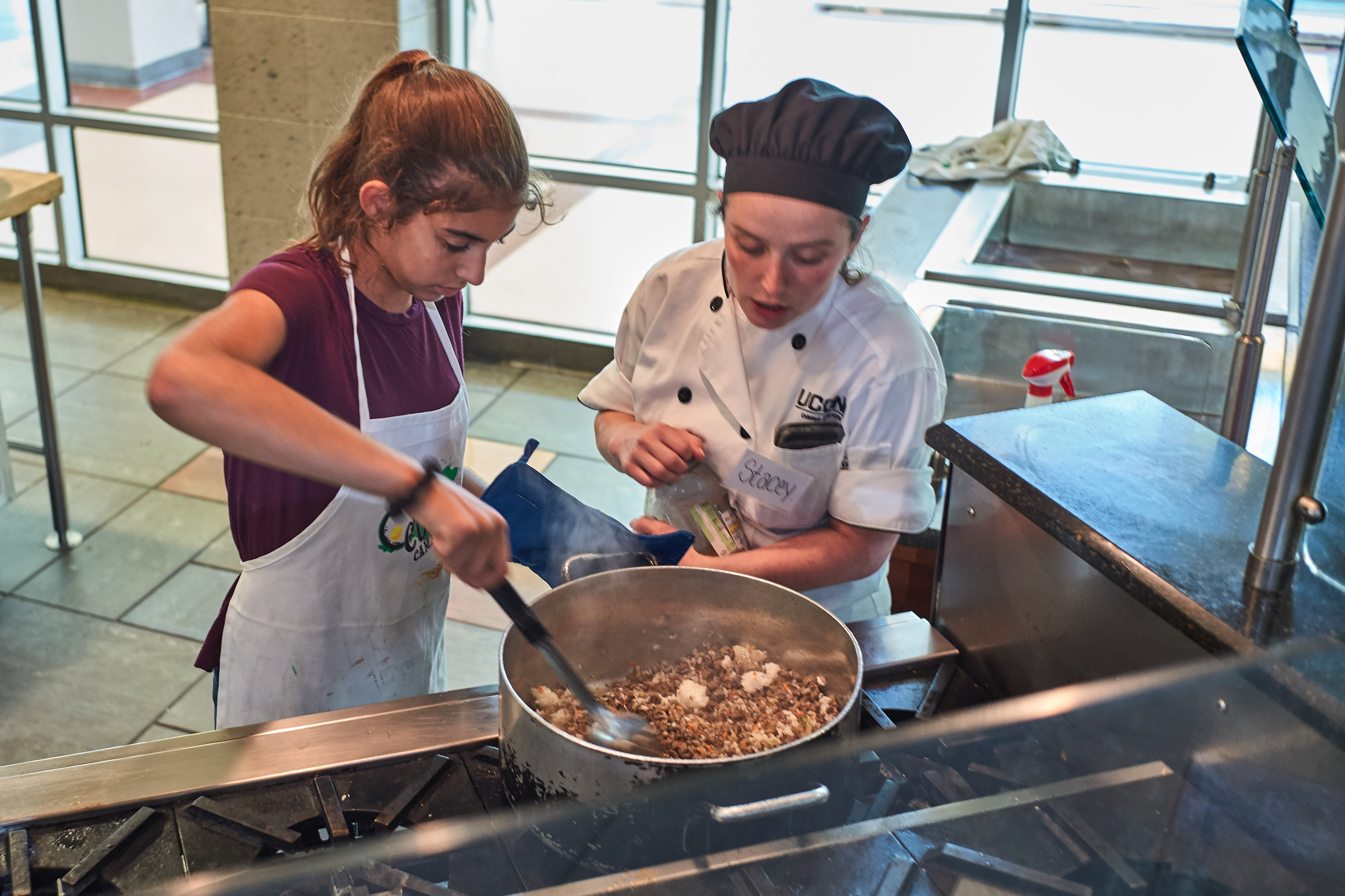 Scarlett Pauloski, 13, of Old Saybrook, left, and Chef Stacy Guitard season taco meat for a main dish during a competition held at the UCann Cook Camp at Gelfenbien Commons on July 18, 2019. (Peter Morenus/UConn Photo)
