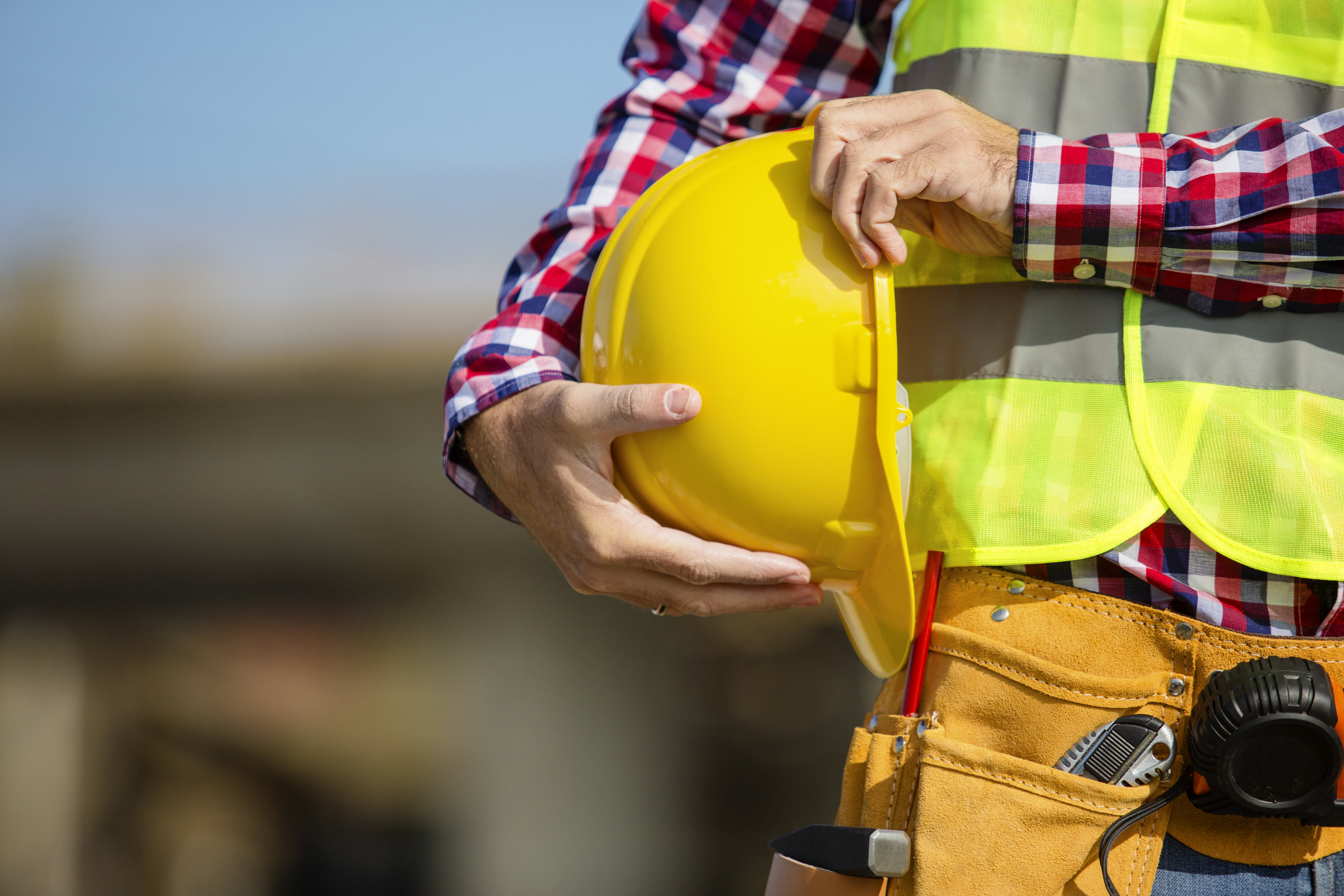 A close-up of a worker holding a yellow hardhat at his side