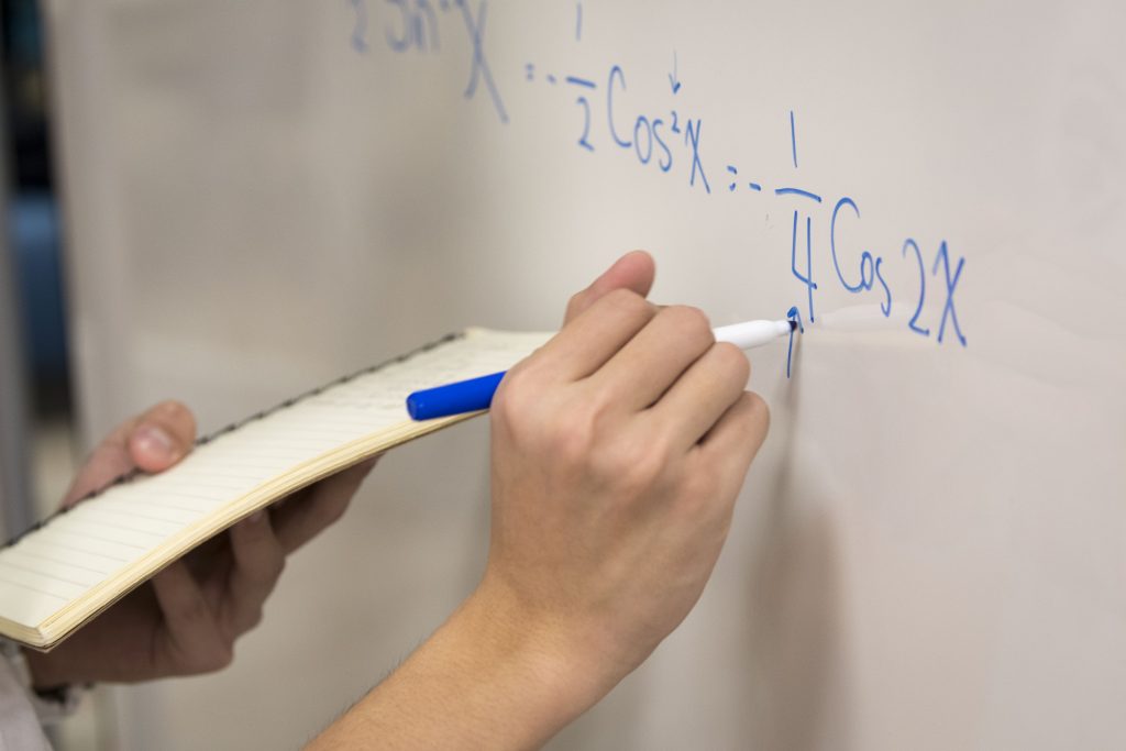 Hand against whiteboard doing math problems.