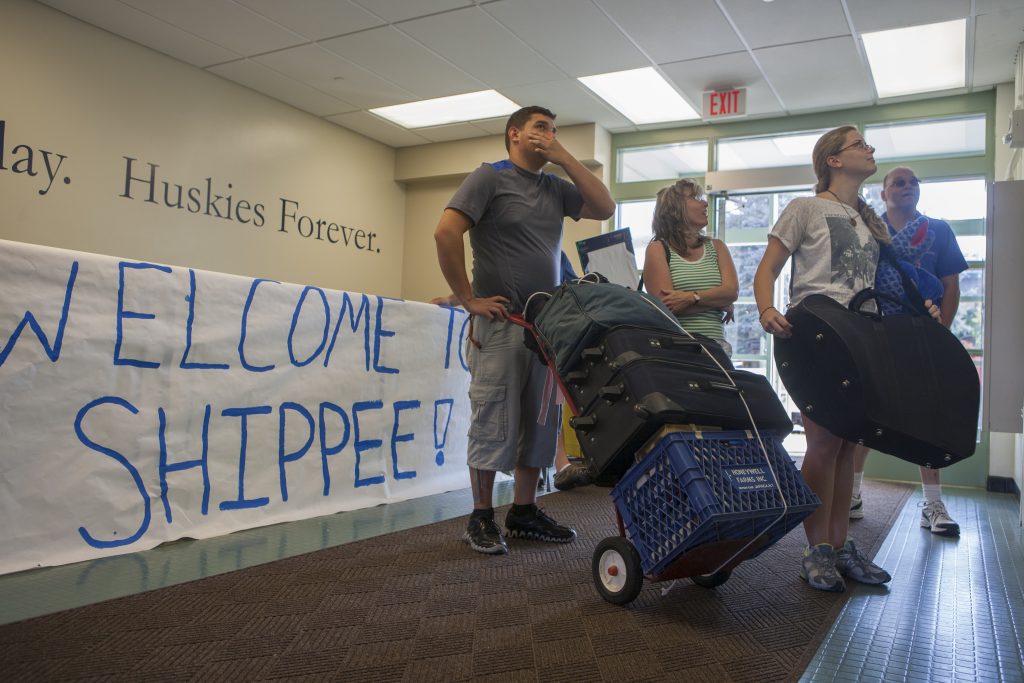 Four people with bags and boxes standing in the lobby of a dorm, with a handpainted sign behind them reading "Welcome to Shippee"