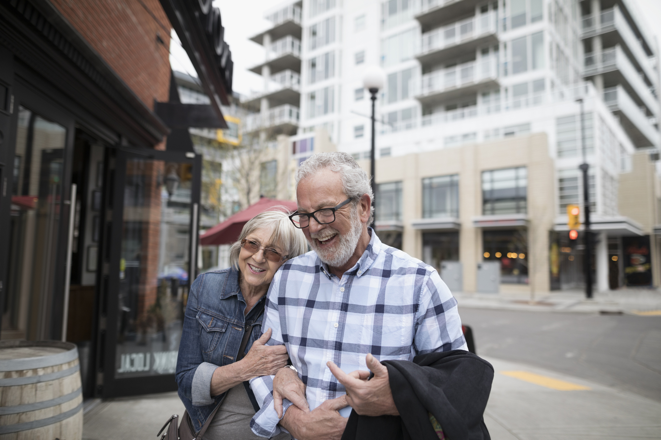 Smiling, affectionate senior couple walking on urban sidewalk