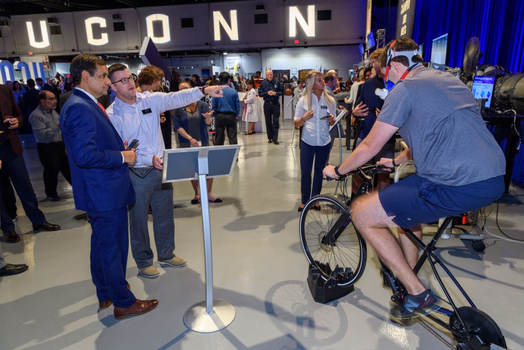 Robert Huggins, center, assistant research professor, explains a Korey Stringer Institute training performance measurement demonstration to Indrajeet Chaubey, CAHNR dean, right. Riding the bicycle is Jeb Struder, a Ph.D. student. (Peter Morenus/UConn Photo)