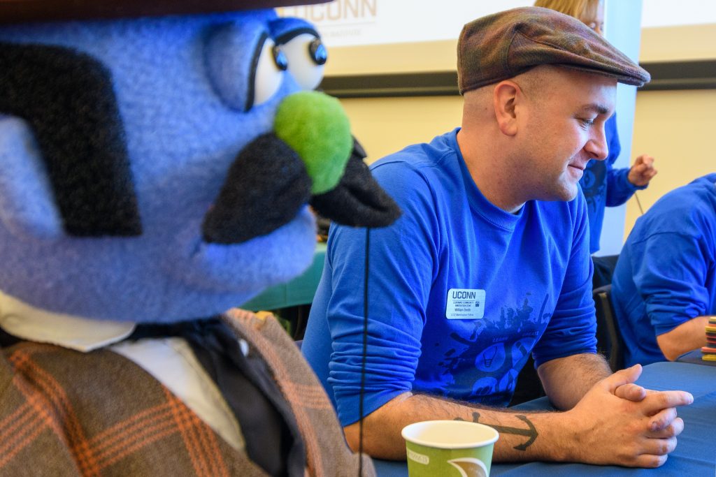A man sits next to a large blue puppet with a mustache and tie, as part of an innovation event