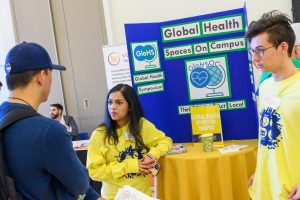 A young woman in front of a display on global health talks with attendees at the UConn Innovation Expo