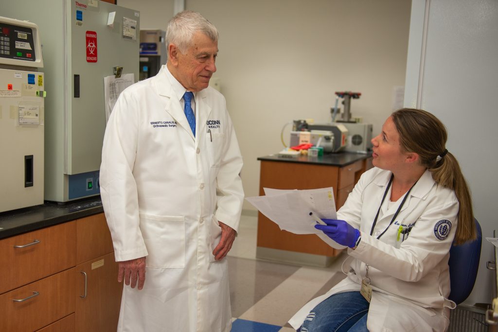 Caucasian male physician, standing, with seated female lab technician.