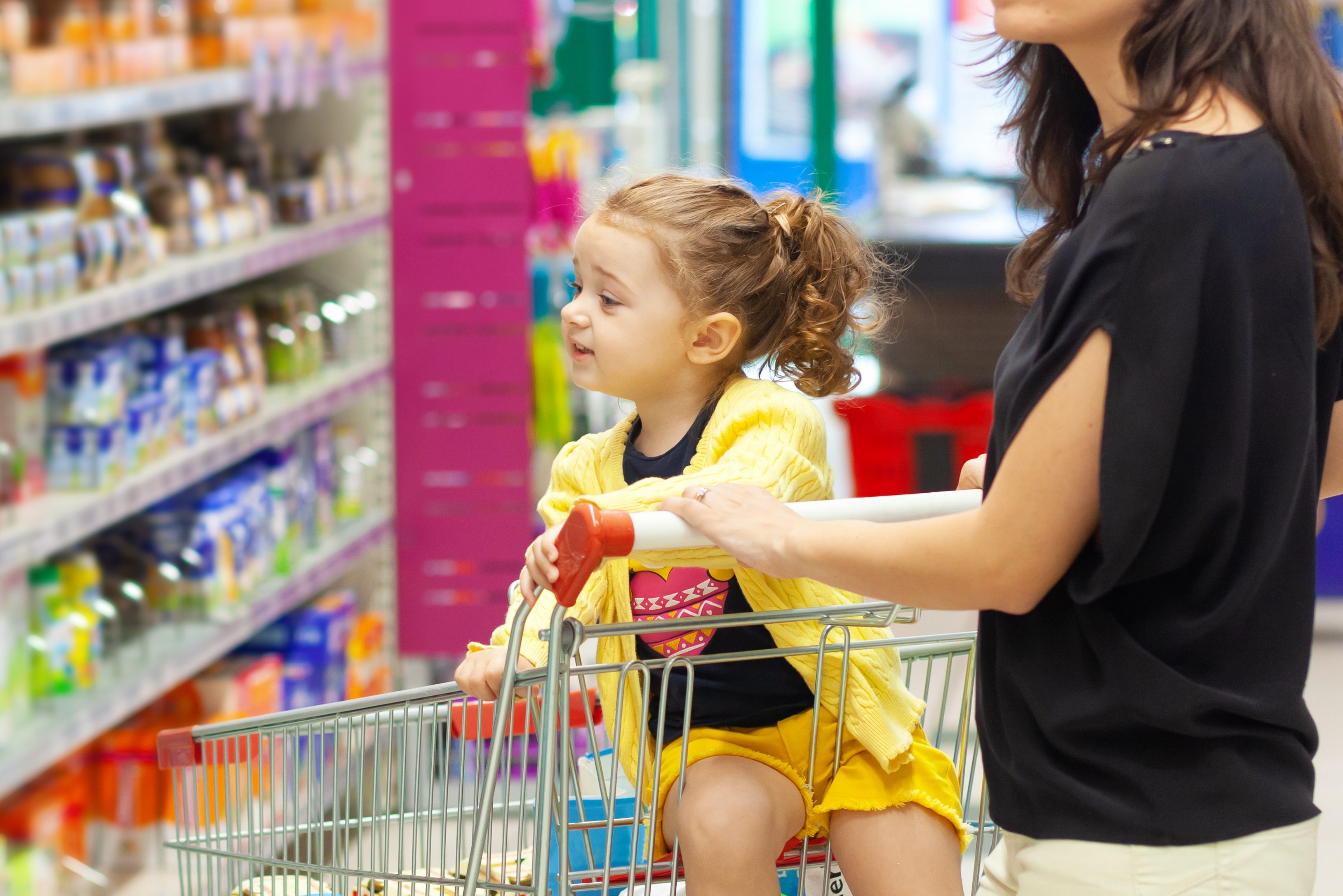 Child looks at grocery shelf selection from a shopping cart. (Shutterstock Image)
