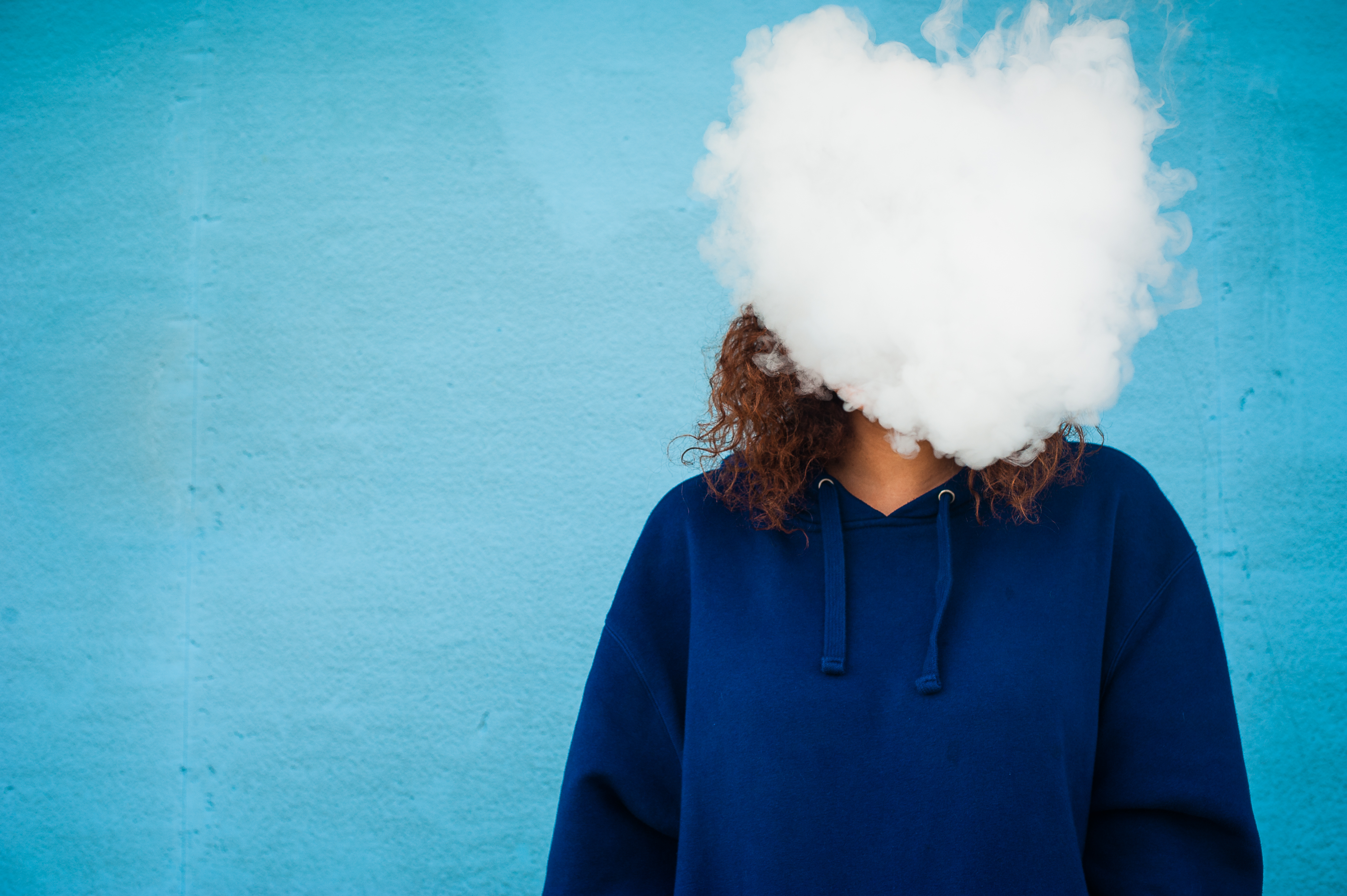 A woman's face is completely hidden by a cloud of smoke from her e-cigarette