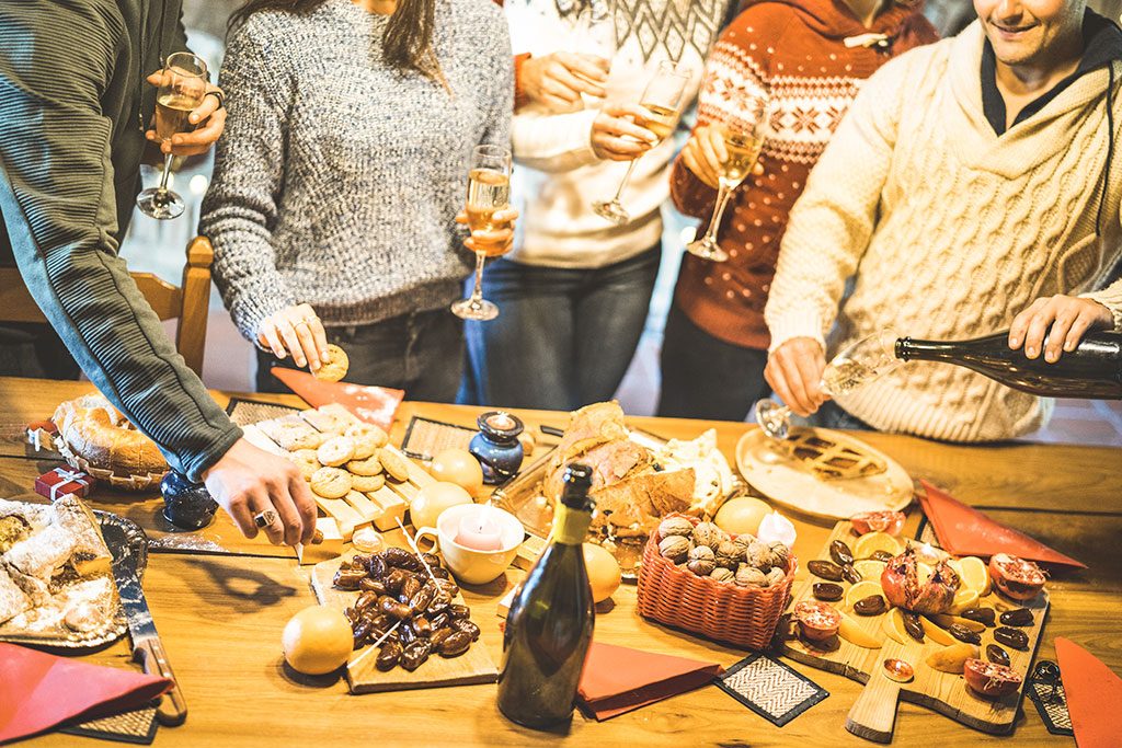 Party-goers with glass of wine in hand around snack table