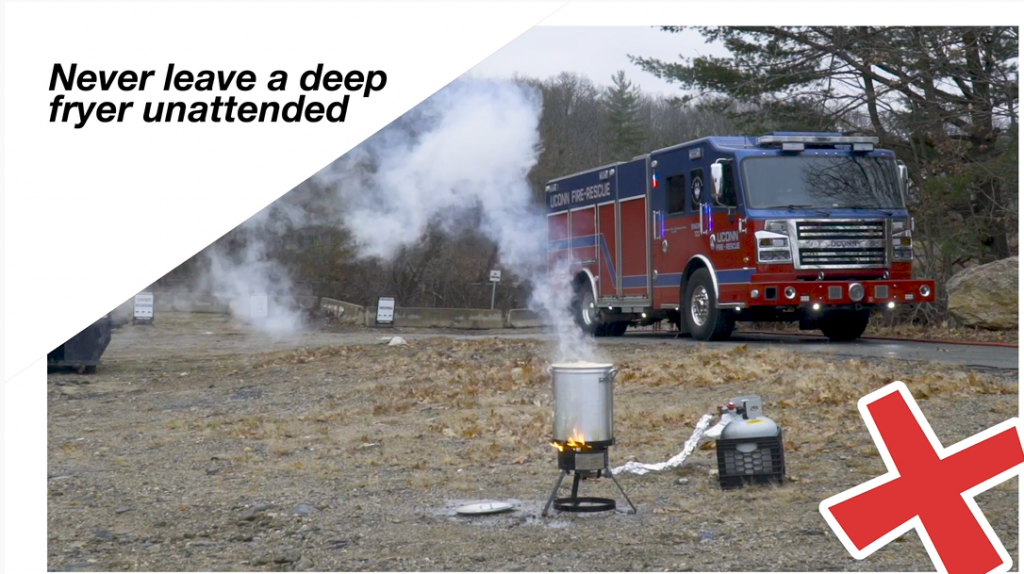 A deep fryer with a turkey inside burns while a UConn fire truck sits in the background.