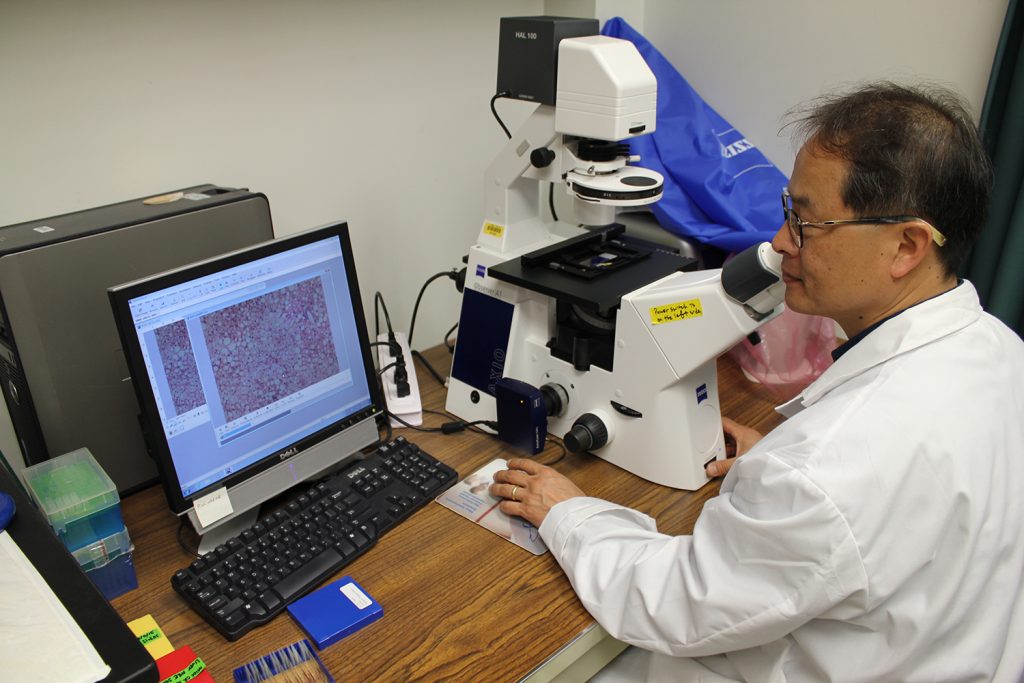 Young-ki Park sitting in front of a microscope and a computer.