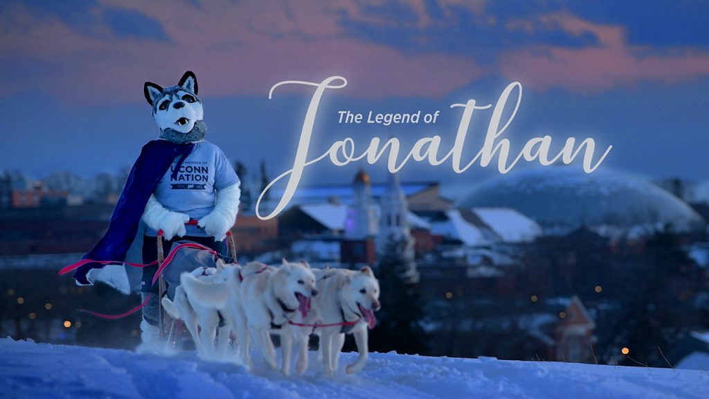 The costumed mascot Jonathan rides a sled pulled by real dogs on a snowy Horsebarn Hill.