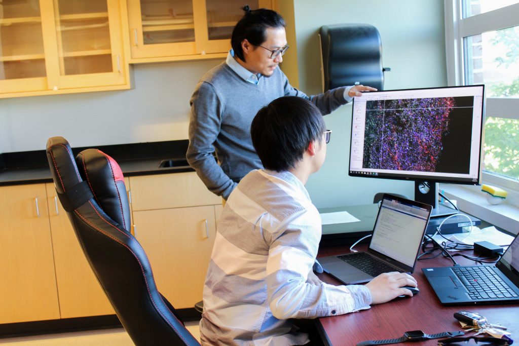 Zhe Zhu and graduate student look at a computer in the lab