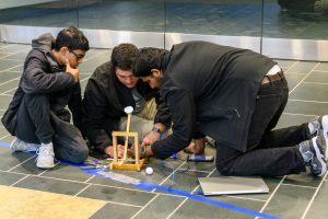 Three students crouched on the floor, working on a model for an engineering project.