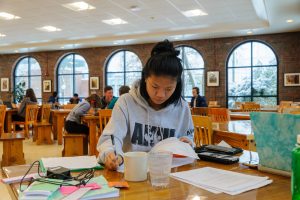 A student studies at a table, with papers spread out before her.