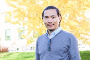 Dr. Zhe Zhu standing outside in front of a tree during autumn