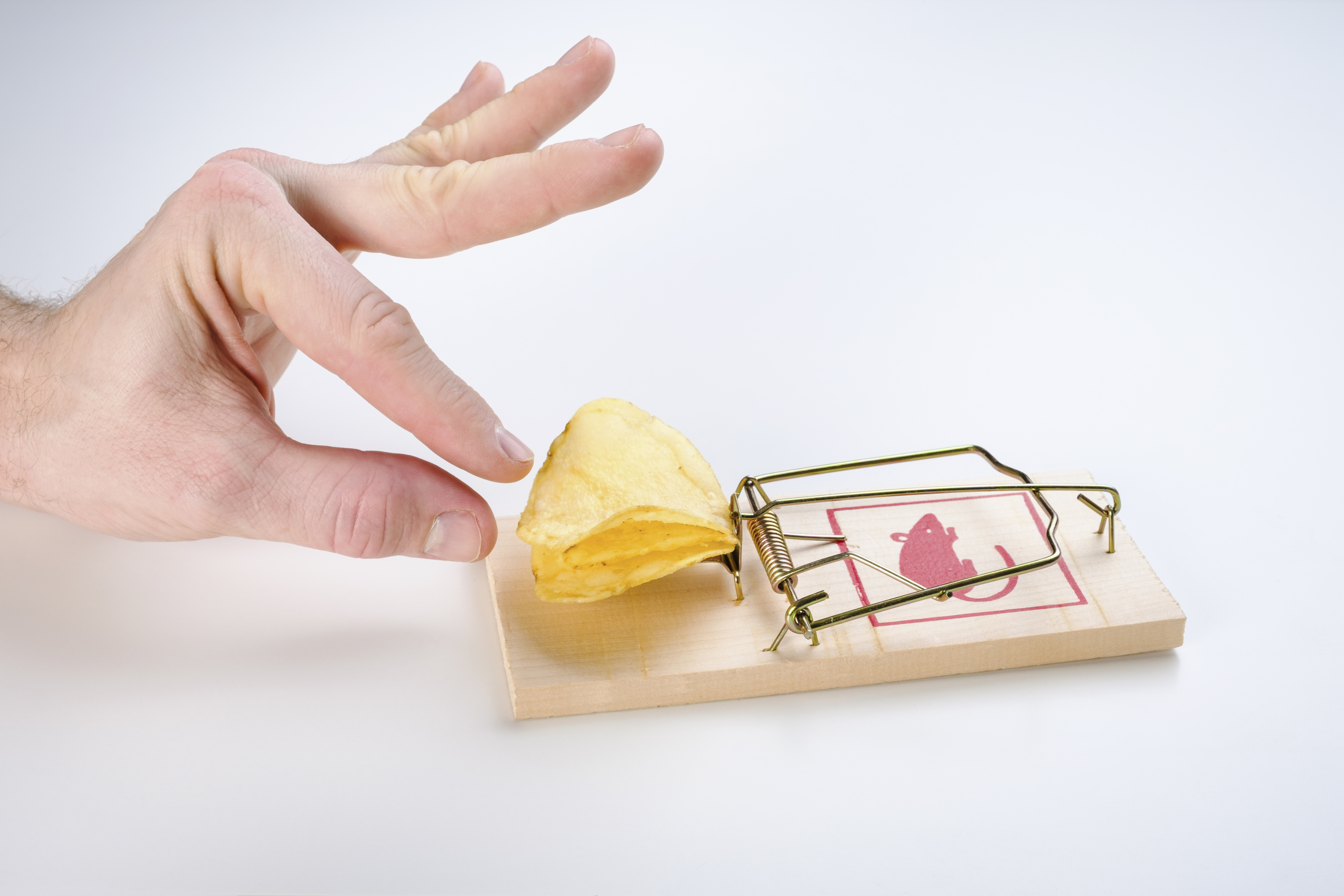A hand reaching for a potato chip that's baiting a mousetrap.