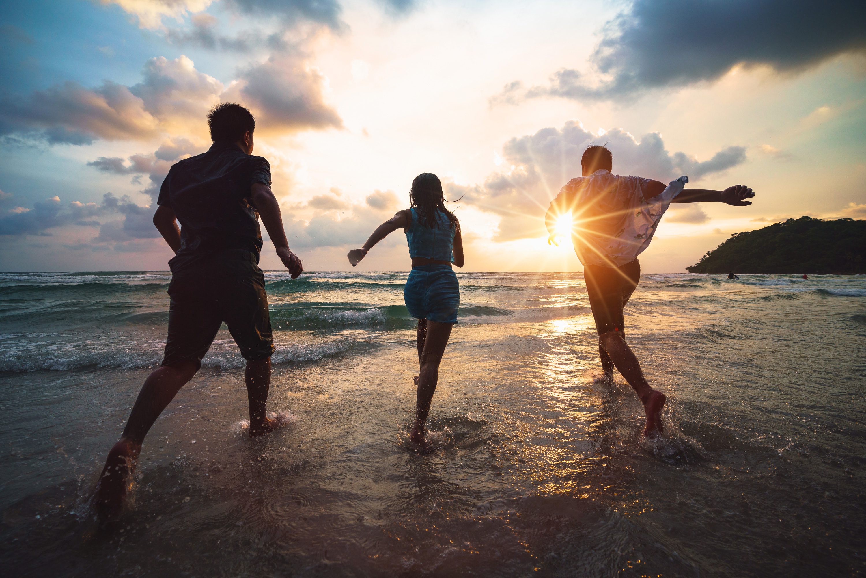 Three people running on a beach at sunset illustrate the idea of happiness.