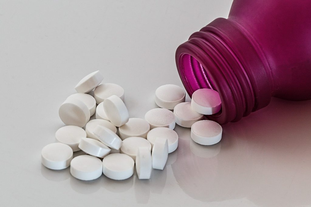 White pills pouring out of a pink prescription bottle