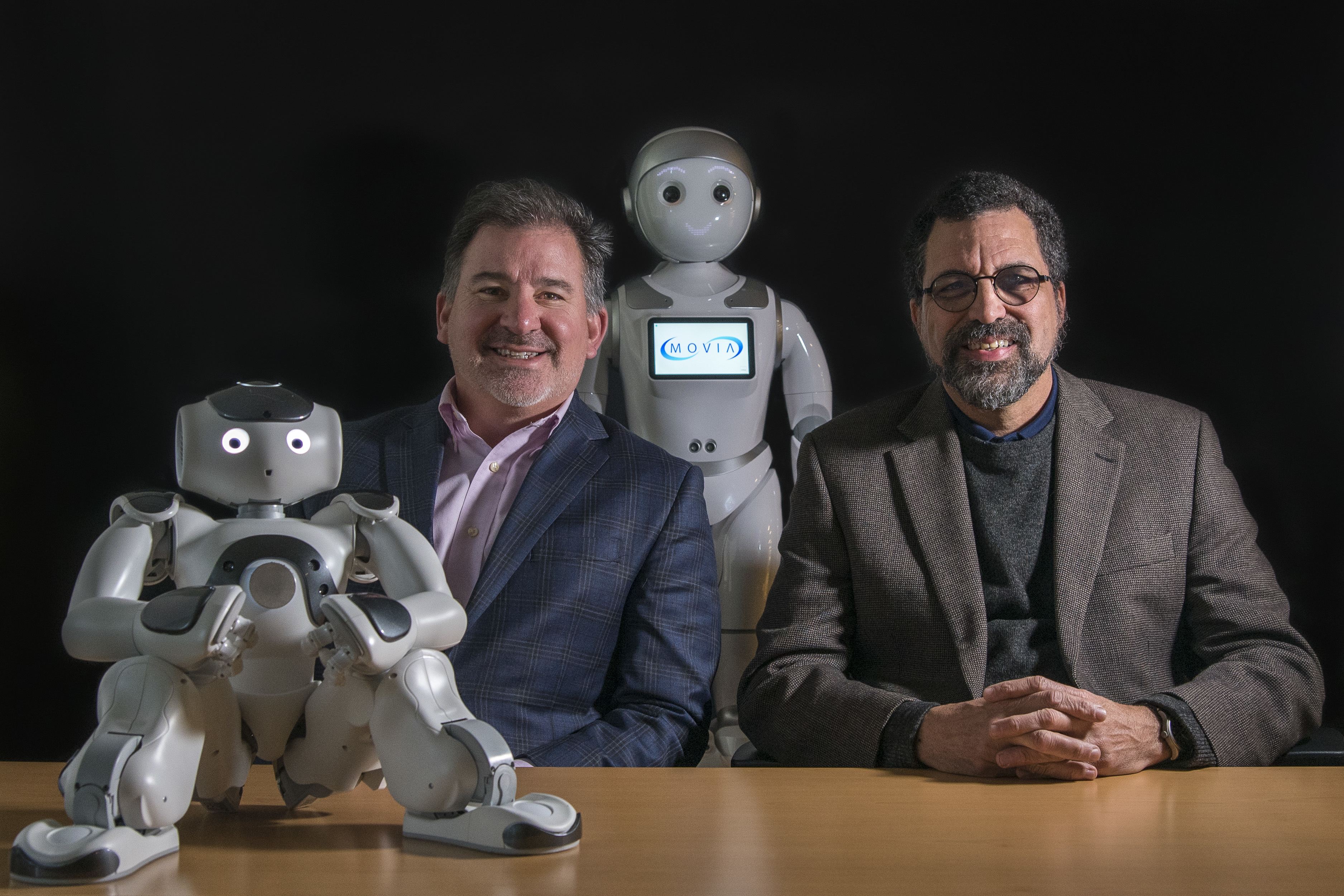 two businessmen sitting with two robots