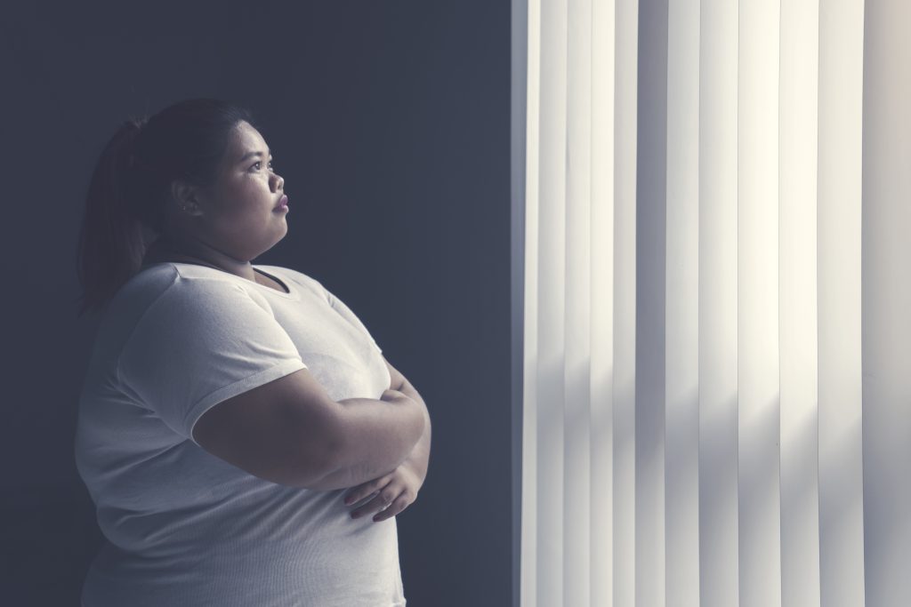 An overweight woman looks out a window