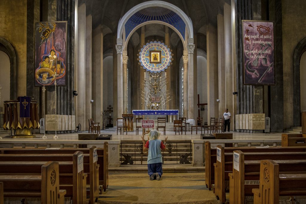A woman kneels in prayer in an empty Catholic cathedral in the Philippines.