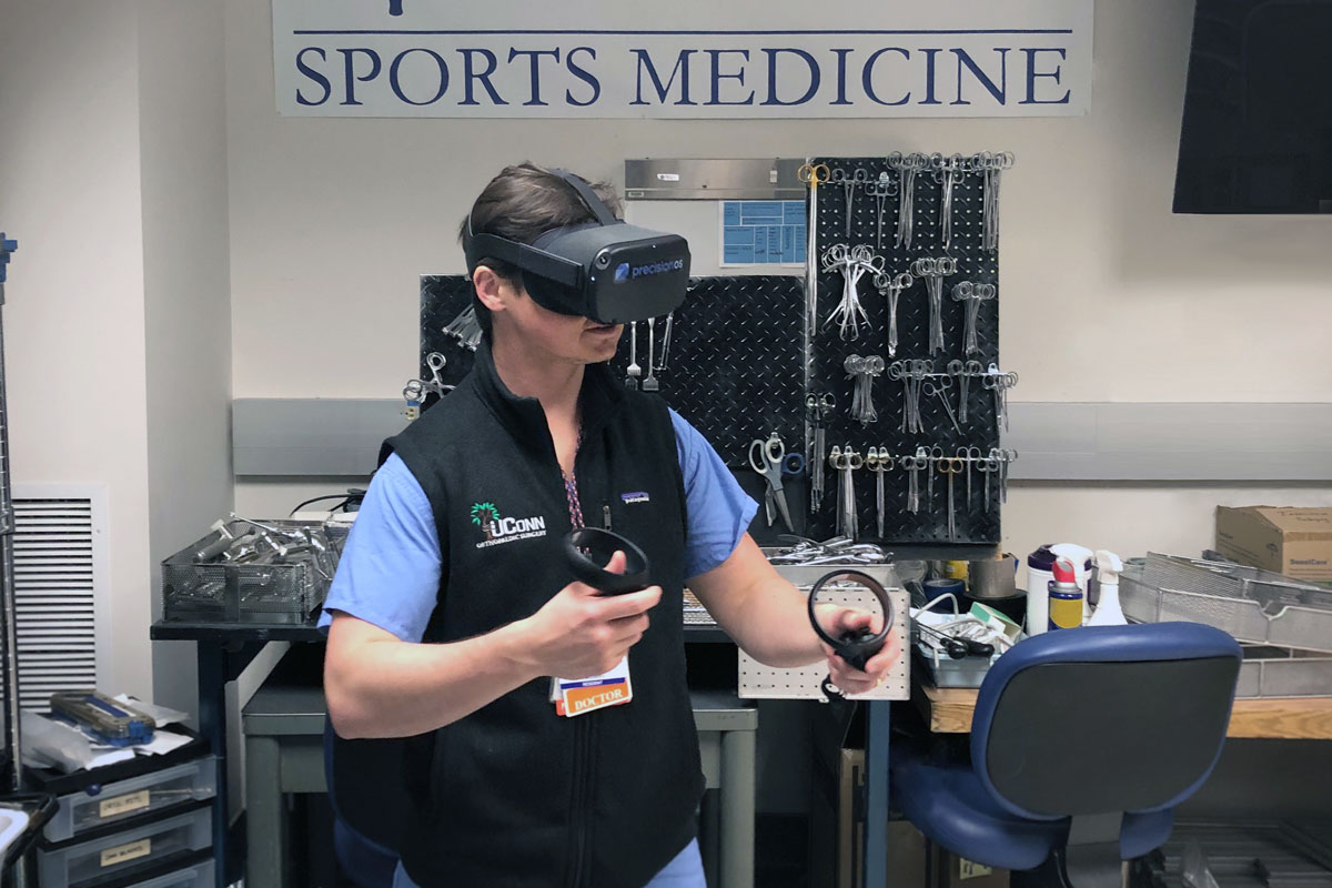 Dr. Merrill wearing virtual reality goggles and holding simulator controllers