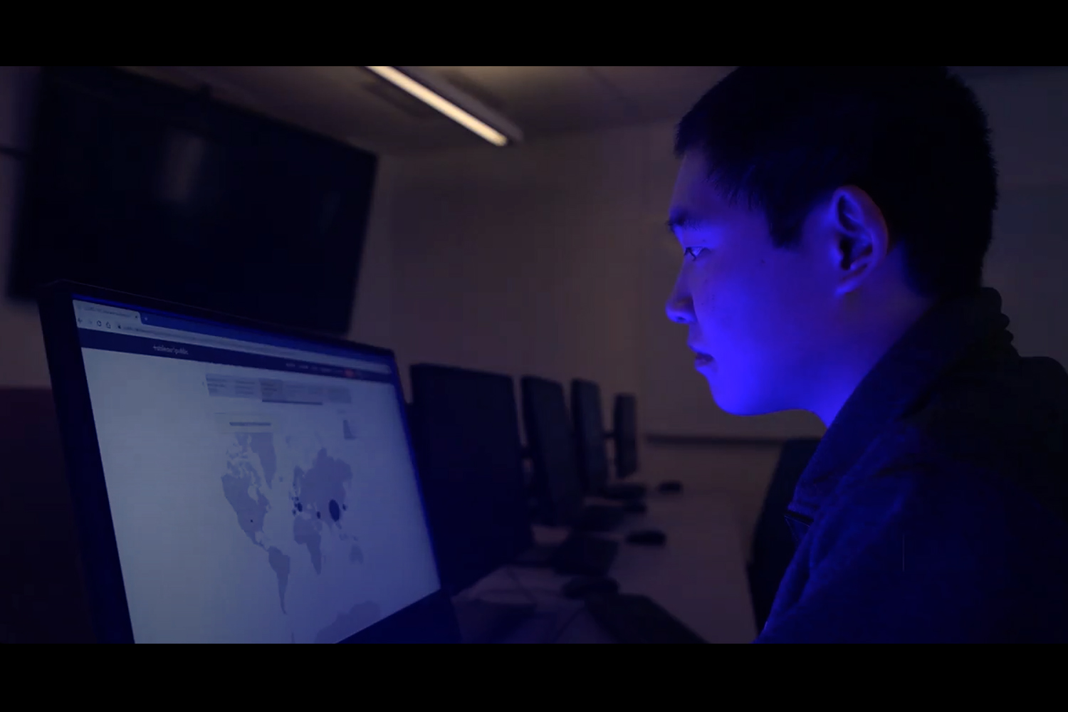 Yuansun (Sonny) Jiang looks at a laptop screen displaying a map of coronavirus cases worldwide in a dark room.