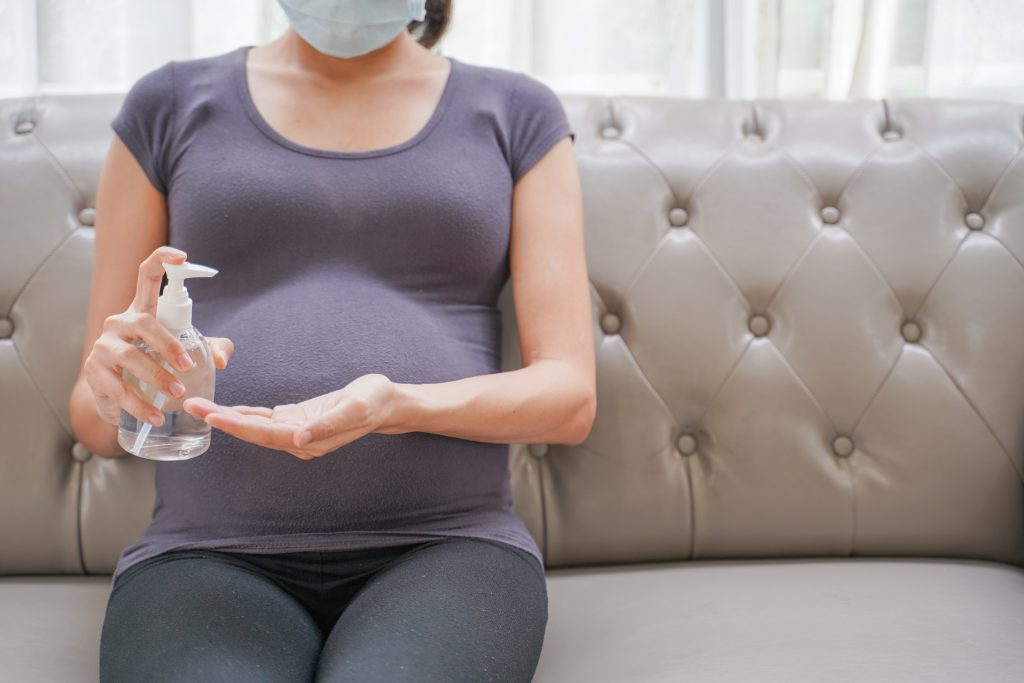 A pregnant woman wearing a medical mask applies sanitizer to her hands.