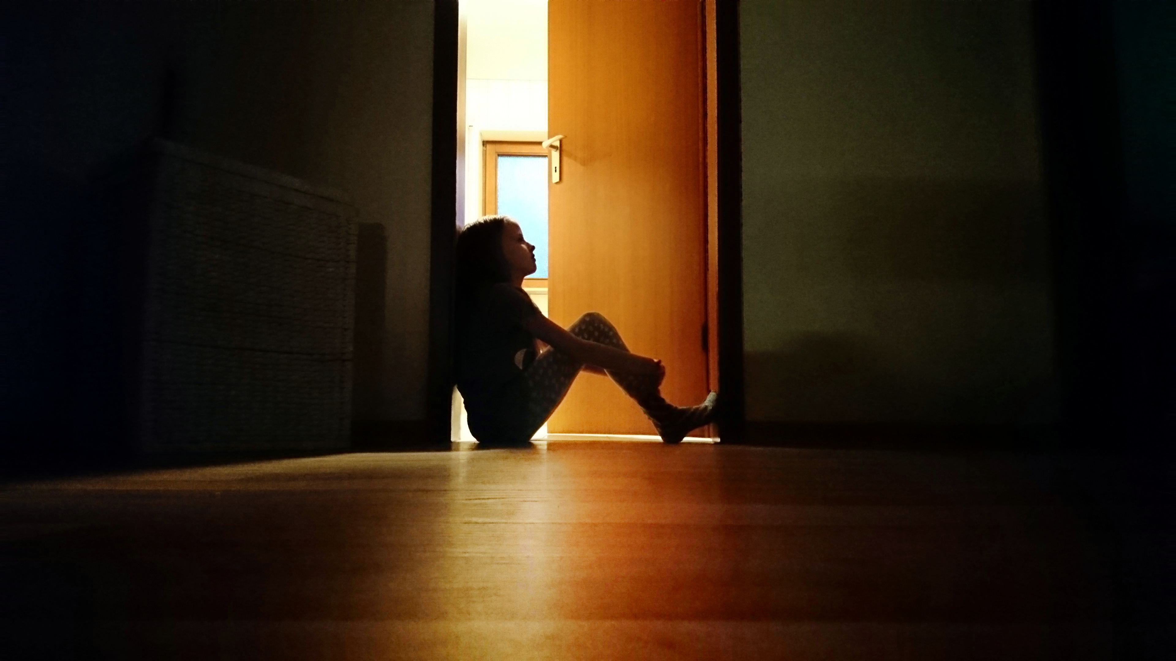 Backlit child sitting in a dark doorway in contemplation