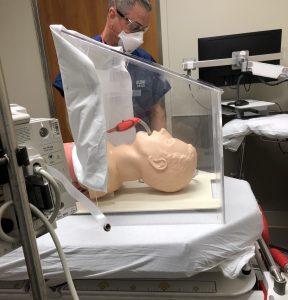 A health care worker looks at a mannequin head displayed inside an intubation hood designed by two UConn Health doctors.