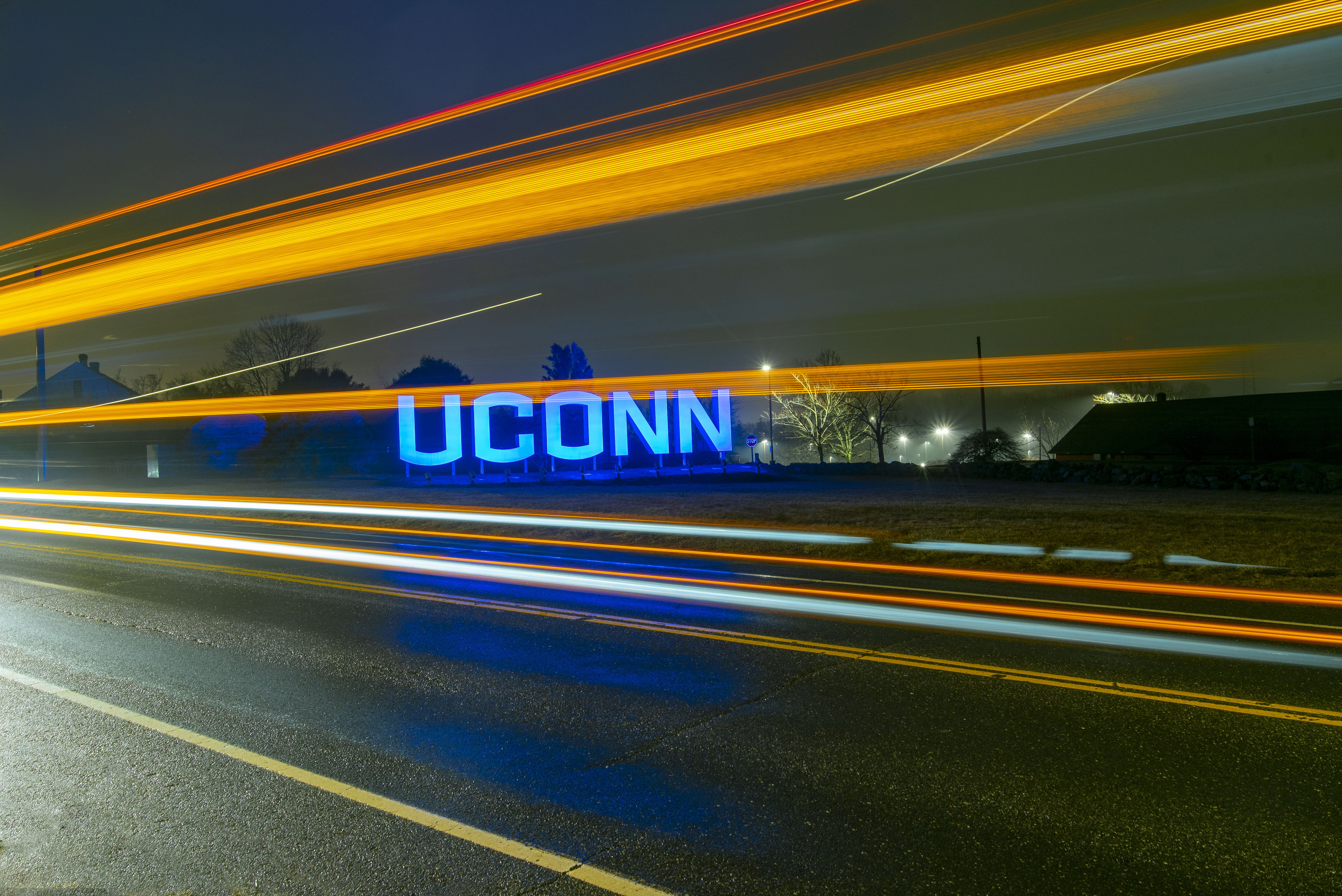 Large UConn sign lit up at night with light trails from car traffic.
