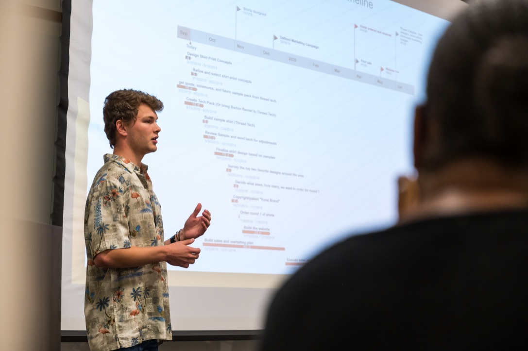 A student, Zac Will, wearing a Hawaiian shirt while making a presentation in front of a class.