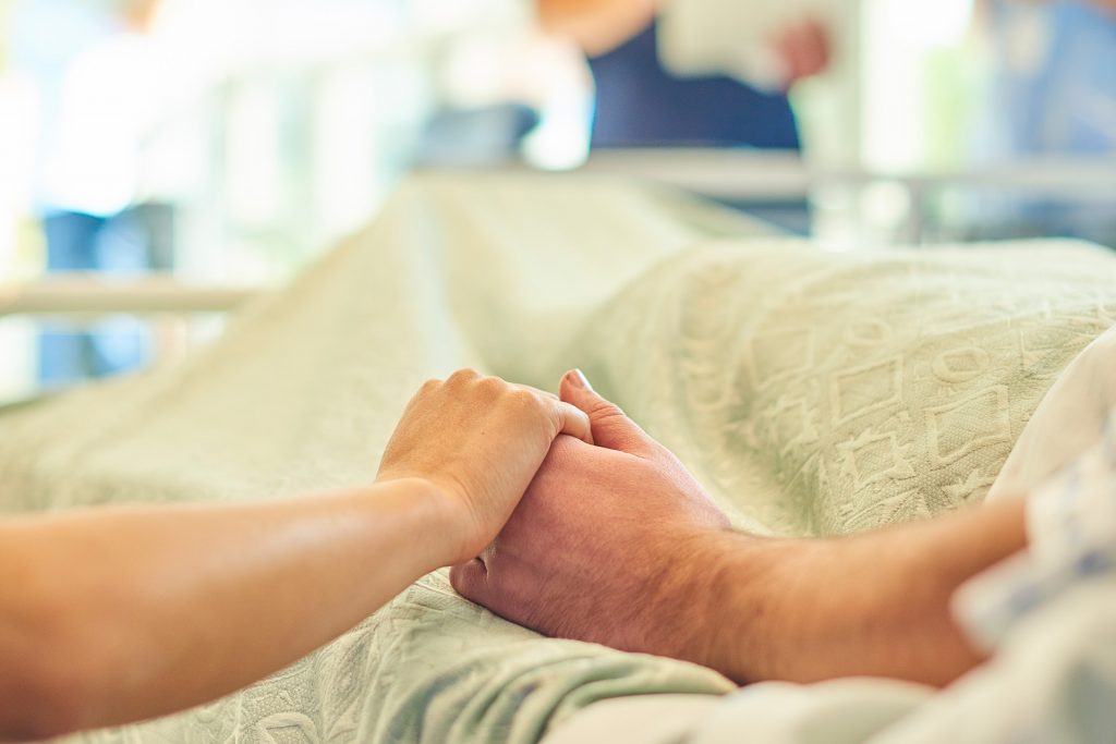 Two people holding hands in a hospital room.