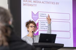 Professor Sherry Pagoto stands in front of a screen displaying a PowerPoint slide, addressing an audience