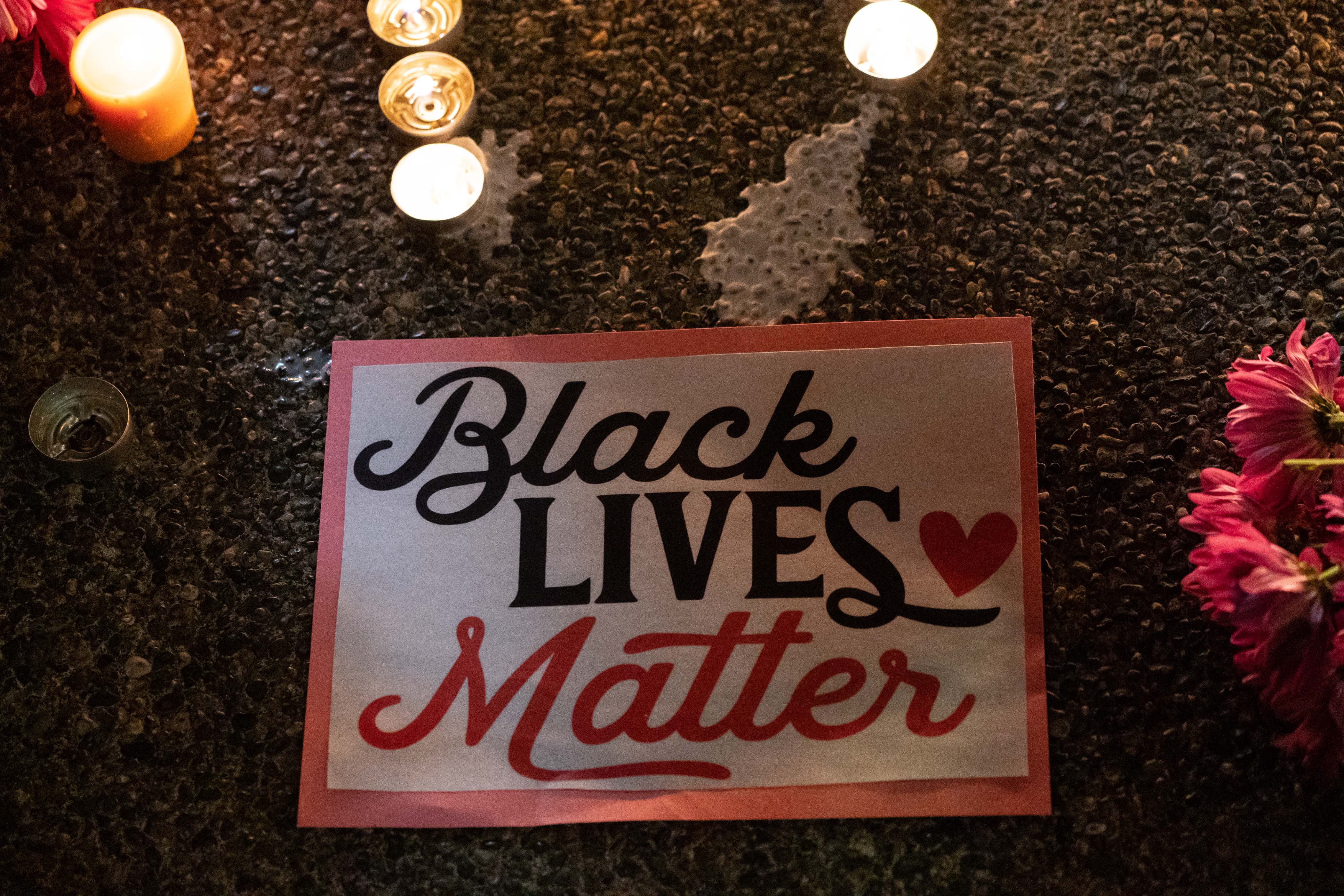 A sign on the ground saying "Black Lives Matter," surrounded by flowers and candles.