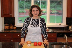 Martina in apron in kitchen with vegetables on a cutting board