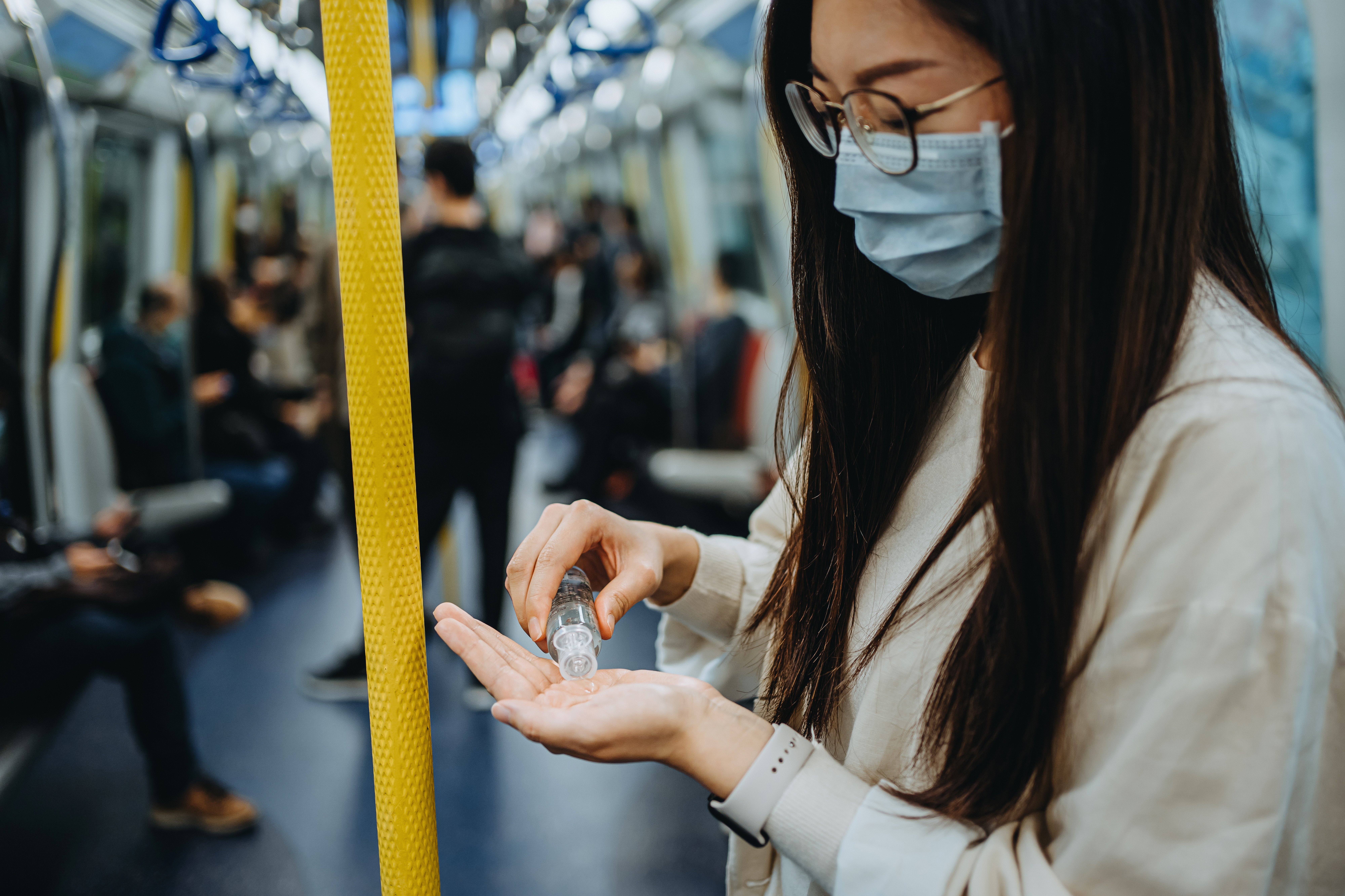 Young woman cleaning hands with alcoholic hand sanitizer to prevent the spread of viruses while commuting in the city riding on subway