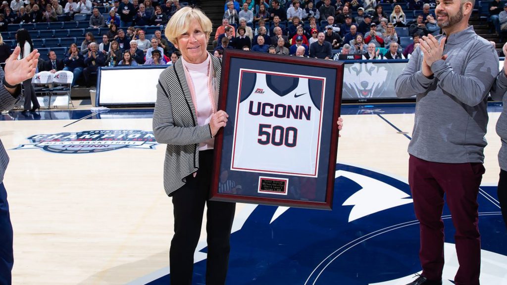 Field hockey coach Nancy Stevens holding a framed jersey with the number 500 on it, a gift she received after her 500th win as a UConn coach