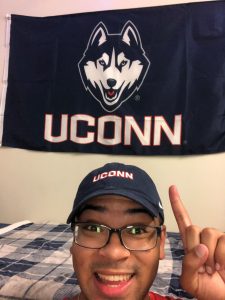 Student RJ Streater takes a selfie in front of a UConn flag in his dorm room