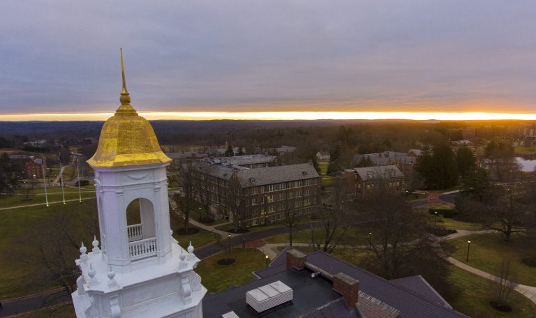 An aerial photo of the gold cupola of the Wilbur Cross building as the sun rises in the horizon