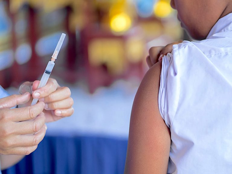 a hand holding a needle and up to a persons arm to give a shot