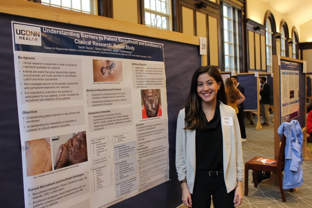 Undergraduate researcher Sarah Tsuruo posing next to a poster documenting some of her research.