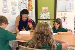 Female teacher works with young students at desk.