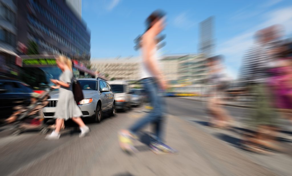 A blurred image of young people crossing a street in front of cars and a bus.