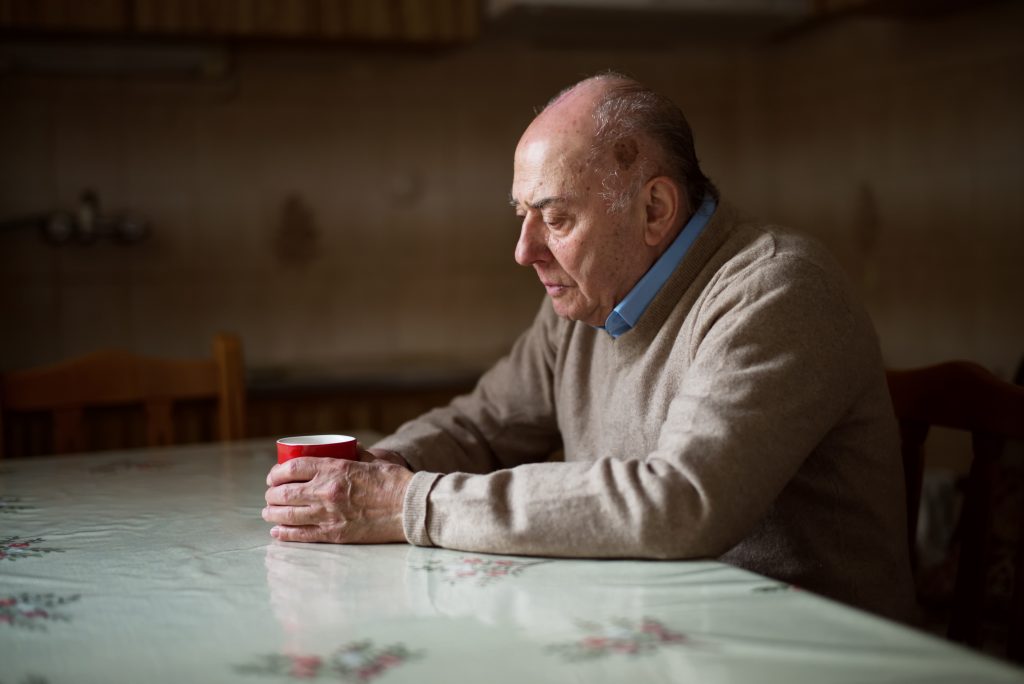 An older man sits alone at a kitchen table, not a soul in the world to so much as ask how his day went