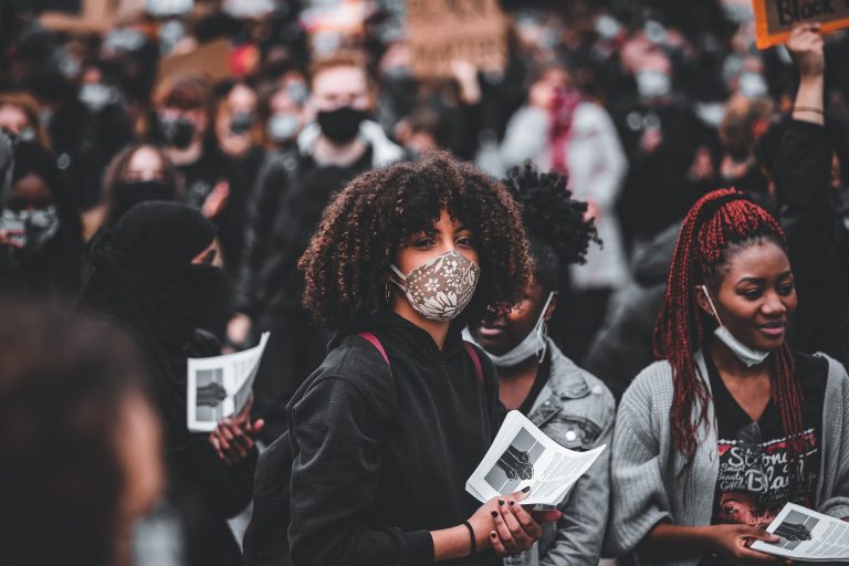 A Black woman wears a face mask in a crowd of people